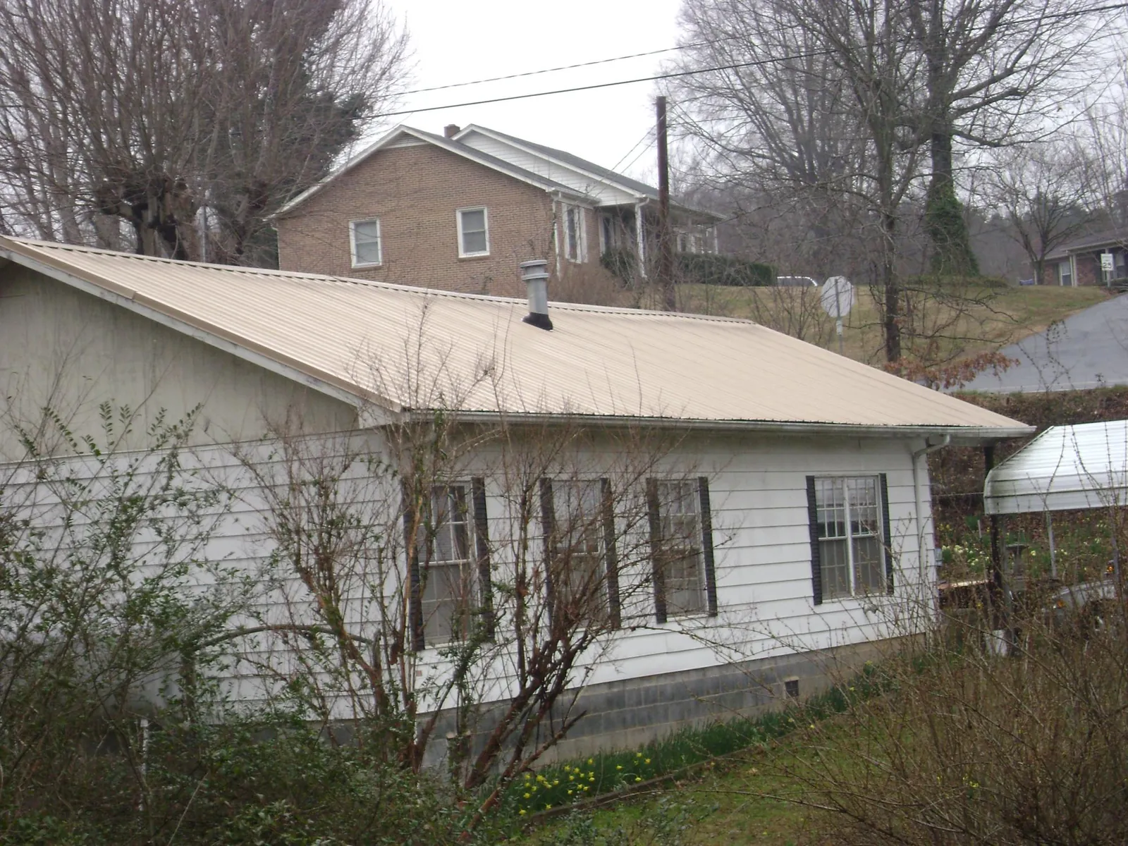Tan metal roof on a white sided house set into a hillside — Commercial Roofing by Roofing Brothers in Mission